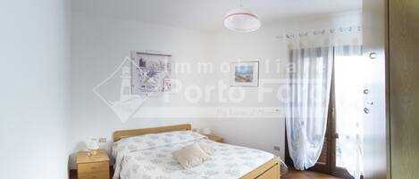 A bedroom with a bed, a bedside table, a hanging light fixture, and a window with curtains.