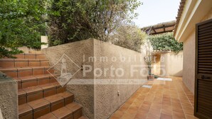 A courtyard with terracotta-tiled steps leading up to a wall, surrounded by greenery and a wooden door. - 16C Appartamento - 16C PORTO MANNU (Palau)