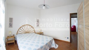 A bedroom with a bed, bedside table, lamp, and a wall-mounted light fixture. - 16B Appartamento - 16B PORTO MANNU (Palau)