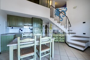 A kitchen with green cabinets, a dining table with chairs, and a staircase with a blue mural. - 18BAIADELFARO - 18 BAIA DEL FARO (Palau)