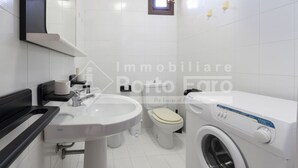 A modern bathroom with a sink, toilet, and washing machine. - 2B Appartamento - 2B PORTO MANNU (Palau)
