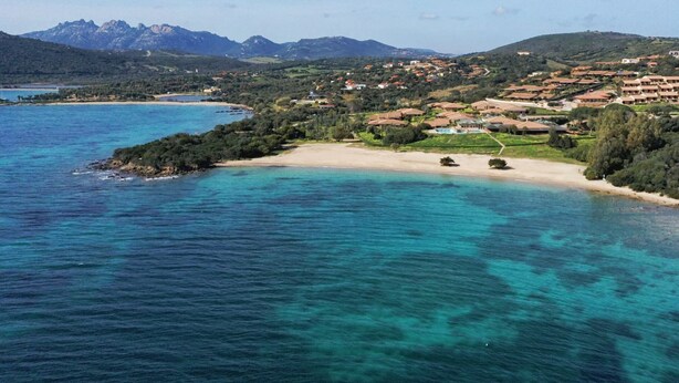 A coastal town with a beach, houses, and mountains in the background. - 2B Appartamento - 2B PORTO MANNU (Palau)