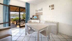 A modern kitchen with a dining area, a TV, and a view of the sea. - 2B Appartamento - 2B PORTO MANNU (Palau)