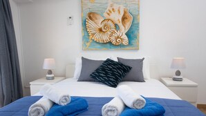 Un letto rifatto con asciugamani blu e bianchi, un cuscino grigio e un'opera d'arte appesa sopra.