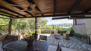 A covered patio with a table and chairs, a ceiling fan, and a view of a lake and hills. - 20E Appartamento - 20E Porto Mannu (Palau)
