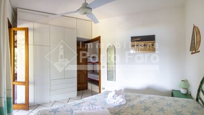 A bedroom with a bed, a ceiling fan, a wardrobe, a small table with a lamp, and a window with a sailboat painting. - 20E Appartamento - 20E Porto Mannu (Palau)