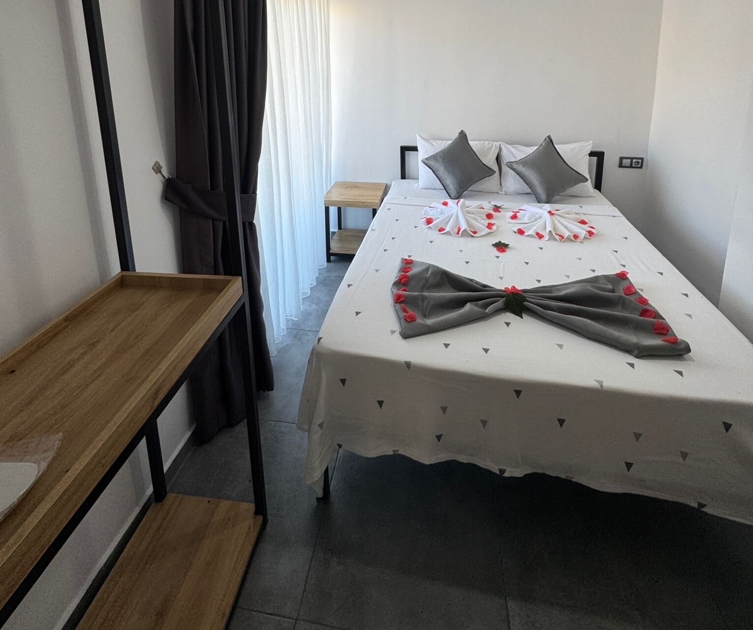 Quarto bem arrumado com uma cama, uma mesinha de madeira e um banquinho.
