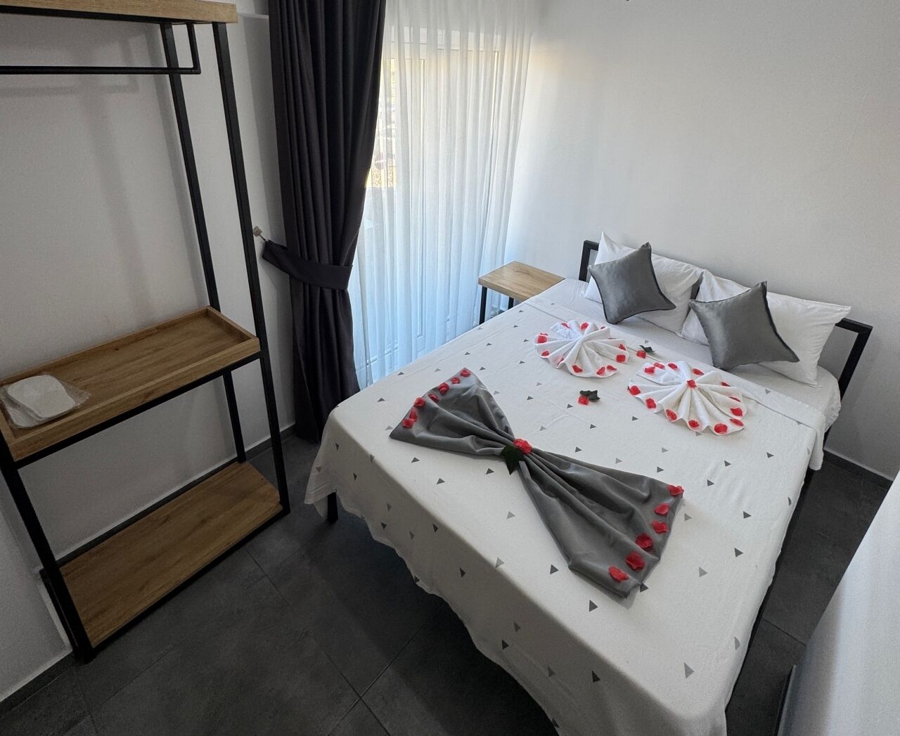 A neatly arranged hotel room with a bed, a small wooden side table, and a shelf unit.