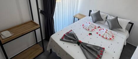 A neatly arranged hotel room with a bed, a small wooden side table, and a shelf unit.