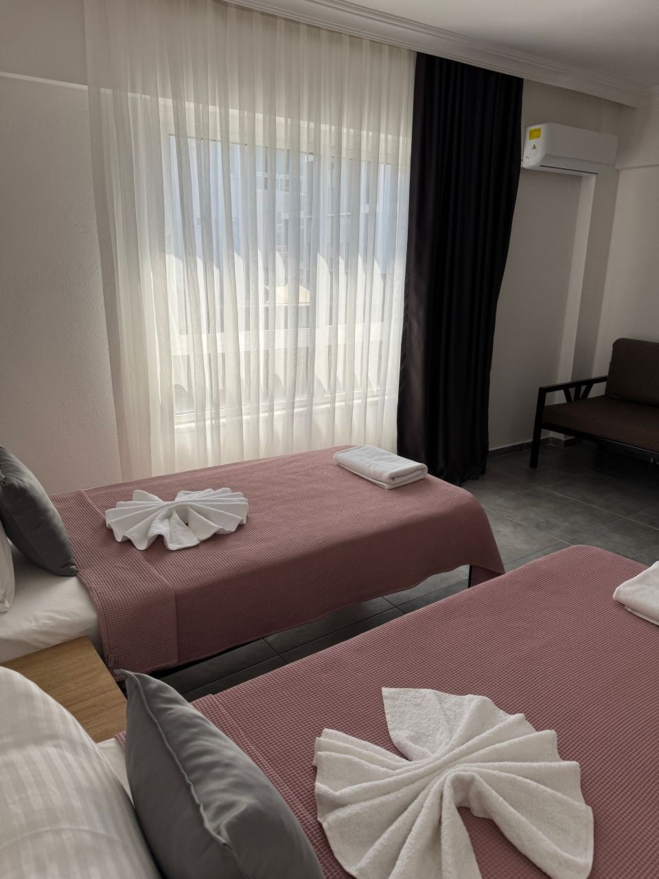 Une chambre d’hôtel avec deux lits, un canapé, une fenêtre avec des rideaux légers et un appareil de climatisation.