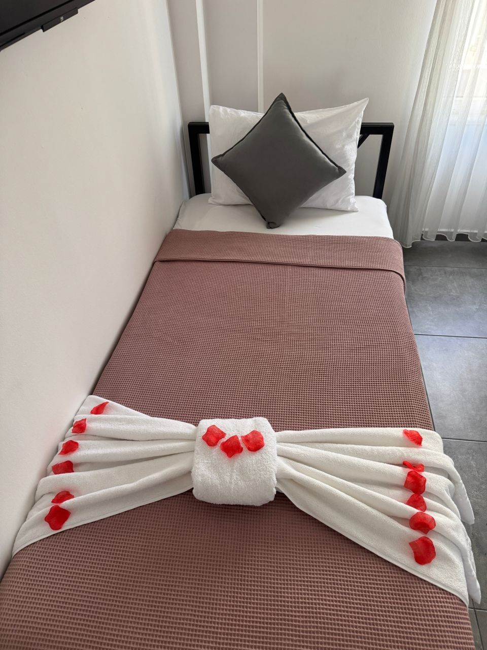 A neatly made bed with a brown bedspread, white pillows, and a decorative towel with red accents.