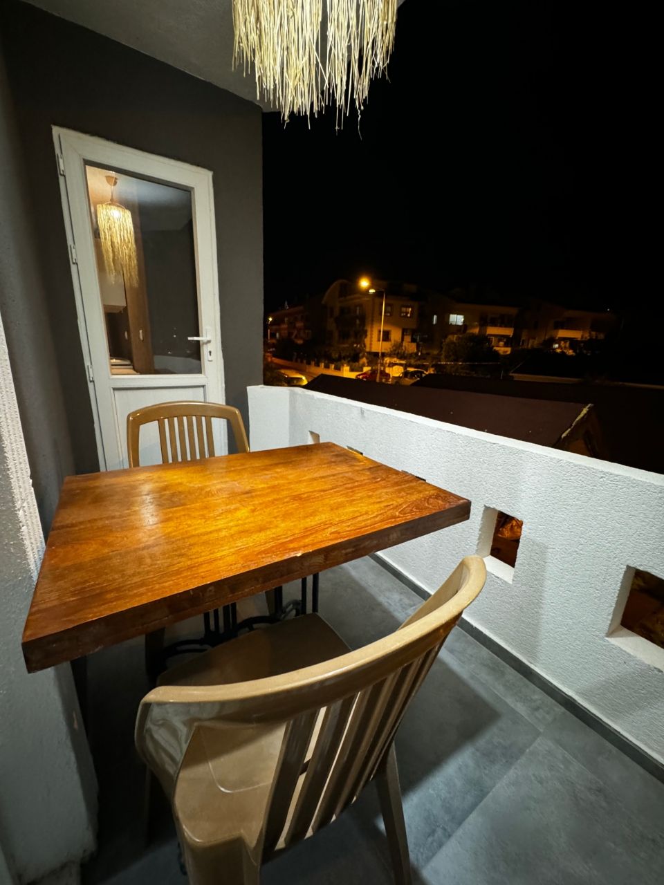 Ein Balkon mit Holztisch und Stühlen, einer Pendelleuchte und Blick auf die beleuchtete Stadt.