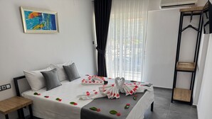 A neatly made bed with a white comforter, gray pillows, and a decorative swan made of towels and rose petals. There is a small wooden nightstand, a black metal shelf unit, and a painting on the wall. - The Pera Hotel Marmaris (Marmaris)