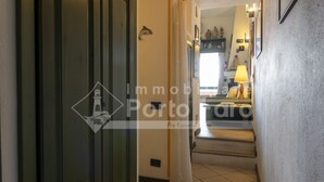 Ein Flur mit Fliesenboden, einer Tür mit Logo und einer Treppe, die zu einem Raum mit Lampe und Regal führt.