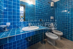 A bathroom with blue tiles, a sink, a toilet, and a bidet.