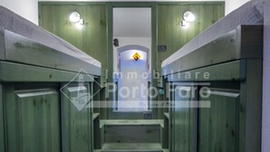 Un pasillo estrecho con paredes de madera y una escalera central que conduce a una puerta con un letrero amarillo en forma de rombo.