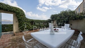 Un patio con una mesa y sillas blancas, una fuente decorativa y vista al mar.