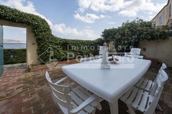 A patio with a white table and chairs, a decorative fountain, and a view of the sea.
