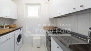 Una cocina moderna con armarios blancos, lavadora integrada, un lavabo y una ventana.