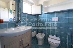 Un bagno con lavandino, mobile, bidet e water, il tutto rivestito di piastrelle blu.