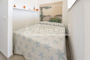 Una camera da letto con un letto coperto da una coperta a motivi stellari, uno scaffale con contenitori arancioni e una pianta sospesa al muro.