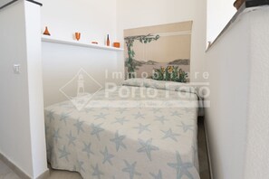 Una camera da letto con un letto ricoperto da una coperta a motivi stellari, un piccolo ripiano con tazze arancioni e un quadro appeso al muro raffigurante un paesaggio.