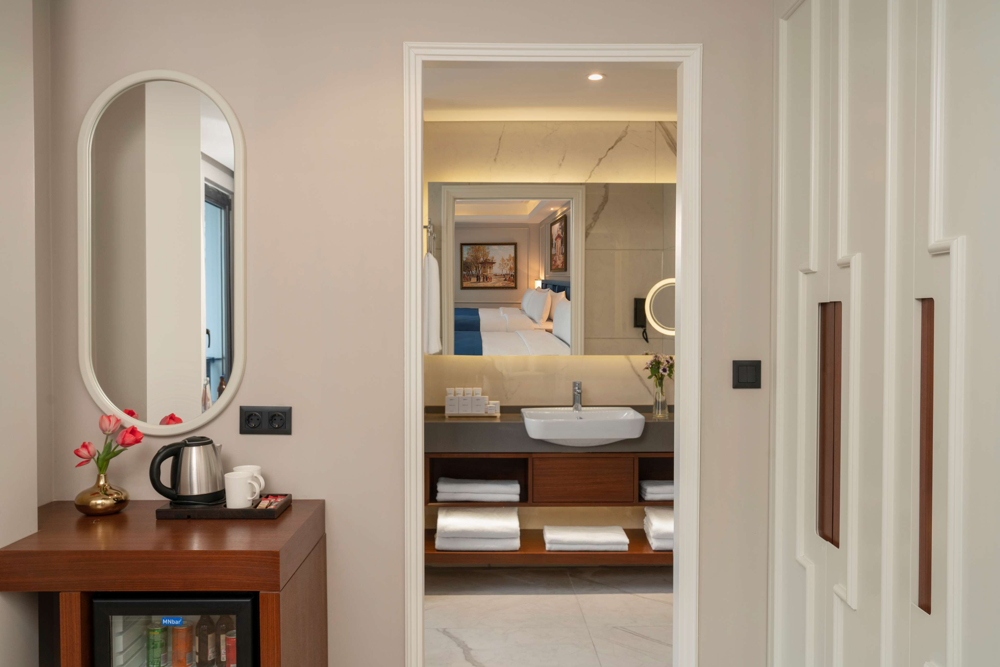 A modern bathroom with a large mirror, a sink, and a vanity with shelves for towels.