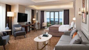 A hotel room with a large bed, a sofa, a desk with a TV, and a view of the city.
