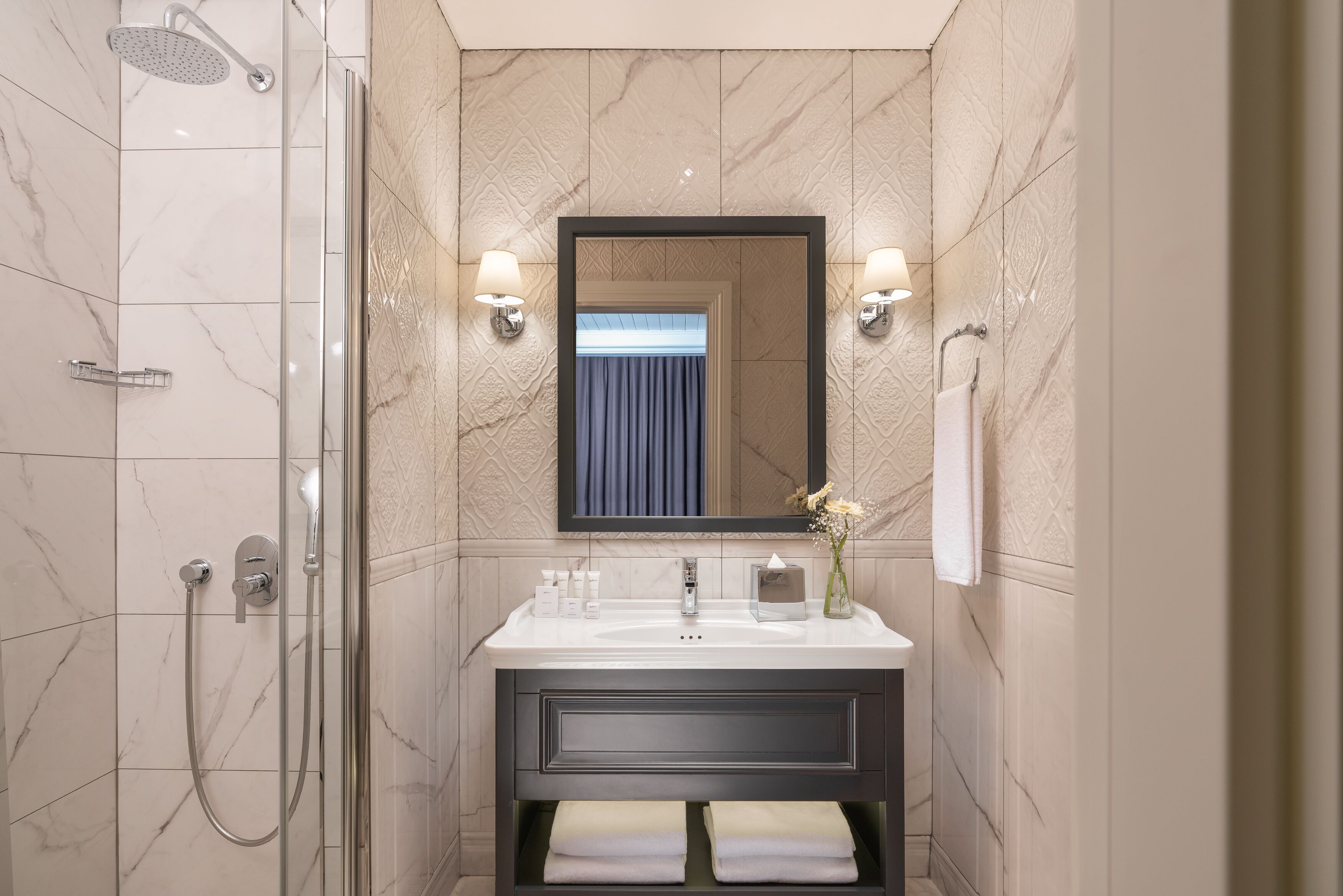 A modern bathroom with a glass-enclosed shower, a large mirror, and a vanity with a sink and towel racks.