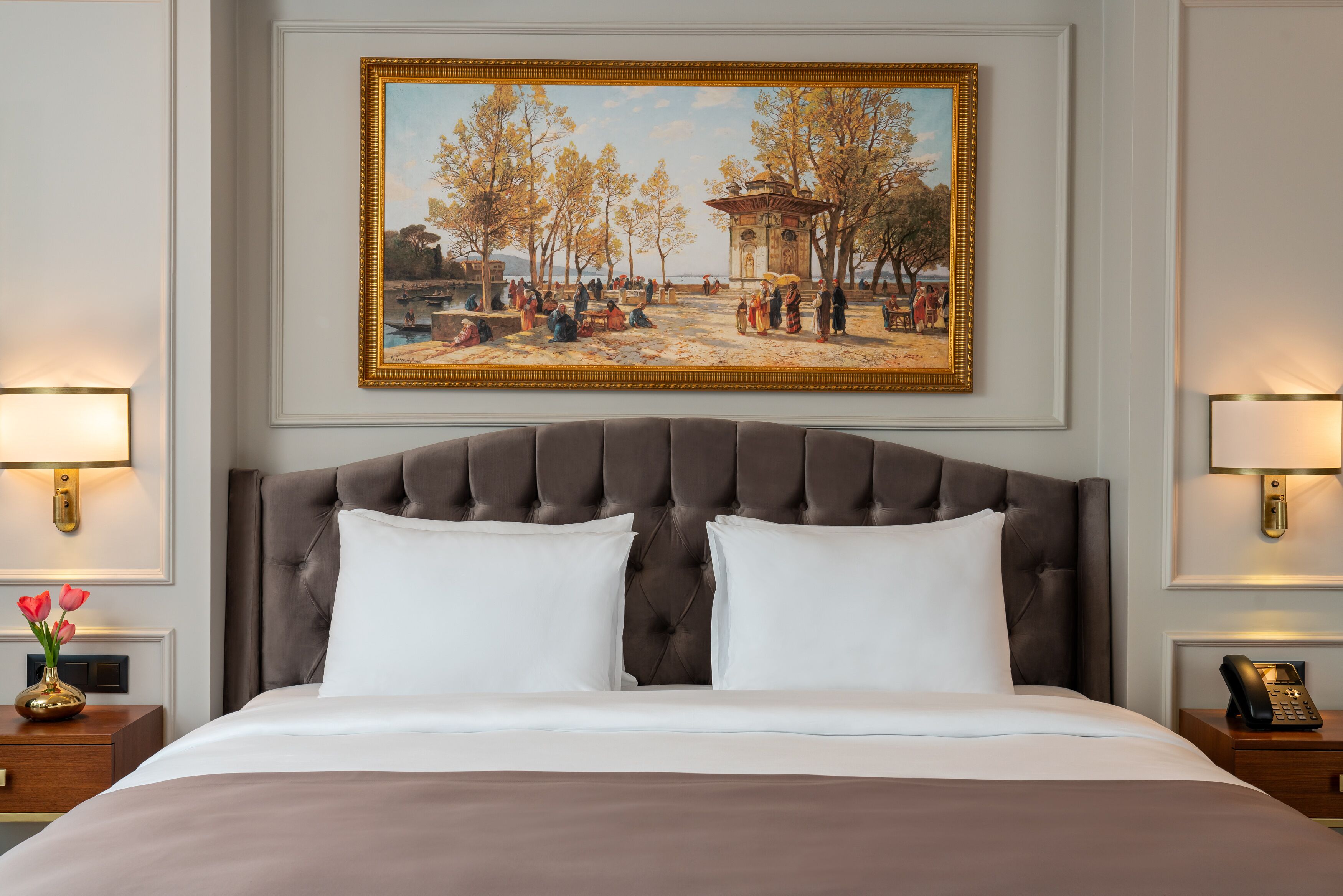 Ein Hotelzimmer mit einem großen Bett, zwei Nachttischen, einem Bild an der Wand und einem Beistelltisch mit Blumen.