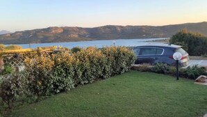 A car parked in a grassy area with a view of a lake and mountains in the background. - L304 Appartamento - L304 PORTO MANNU (Palau)
