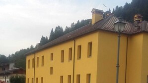 A parking lot with two cars parked in front of a yellow building with multiple windows and a tiled roof. - ex scuola ristrutturata di recente (PAULARO)