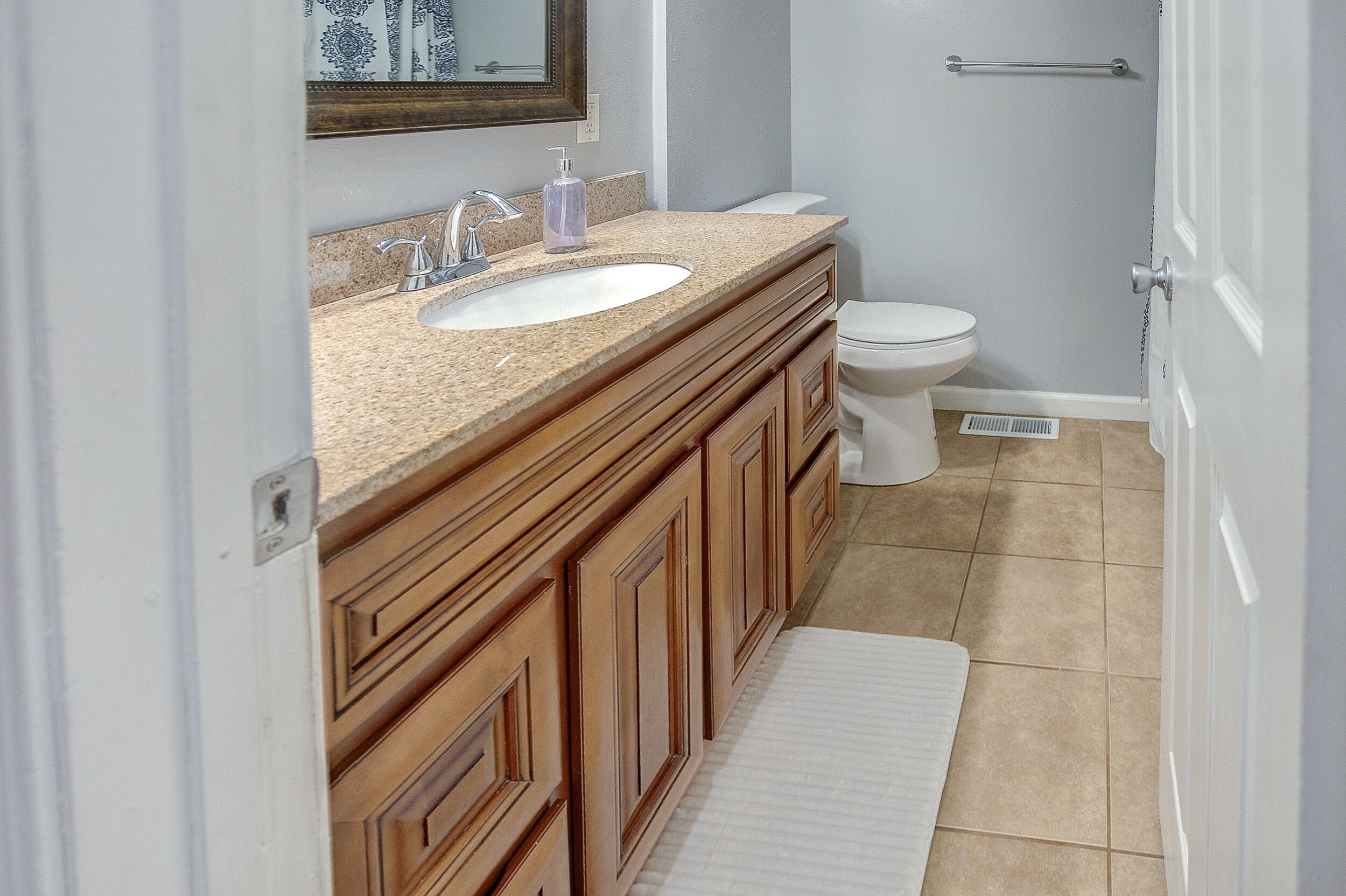 A bathroom with a wooden vanity, a sink, a mirror, a toilet, and a shower area.