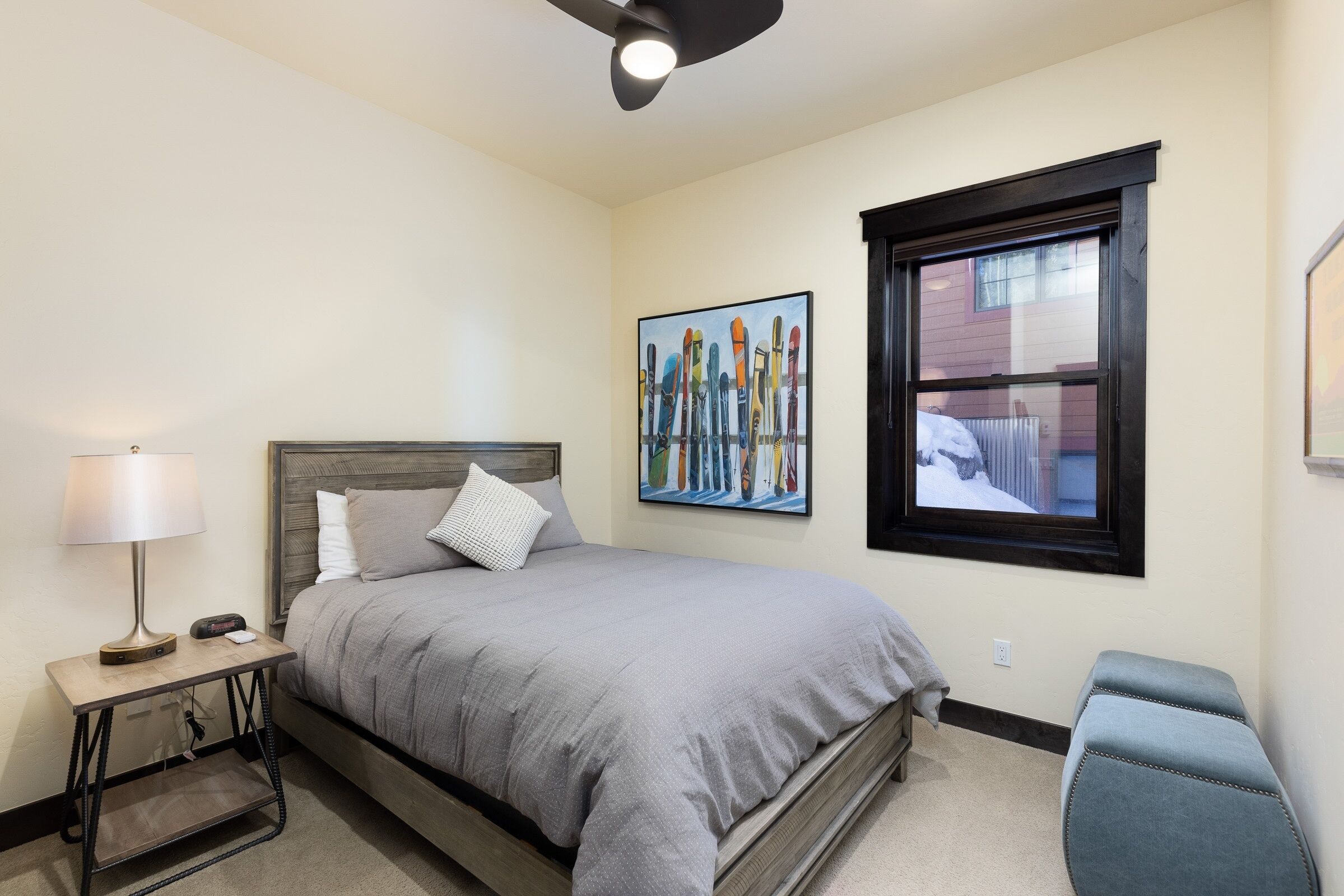 A bedroom with a bed, bedside table, lamp, and a window with a view of a building.