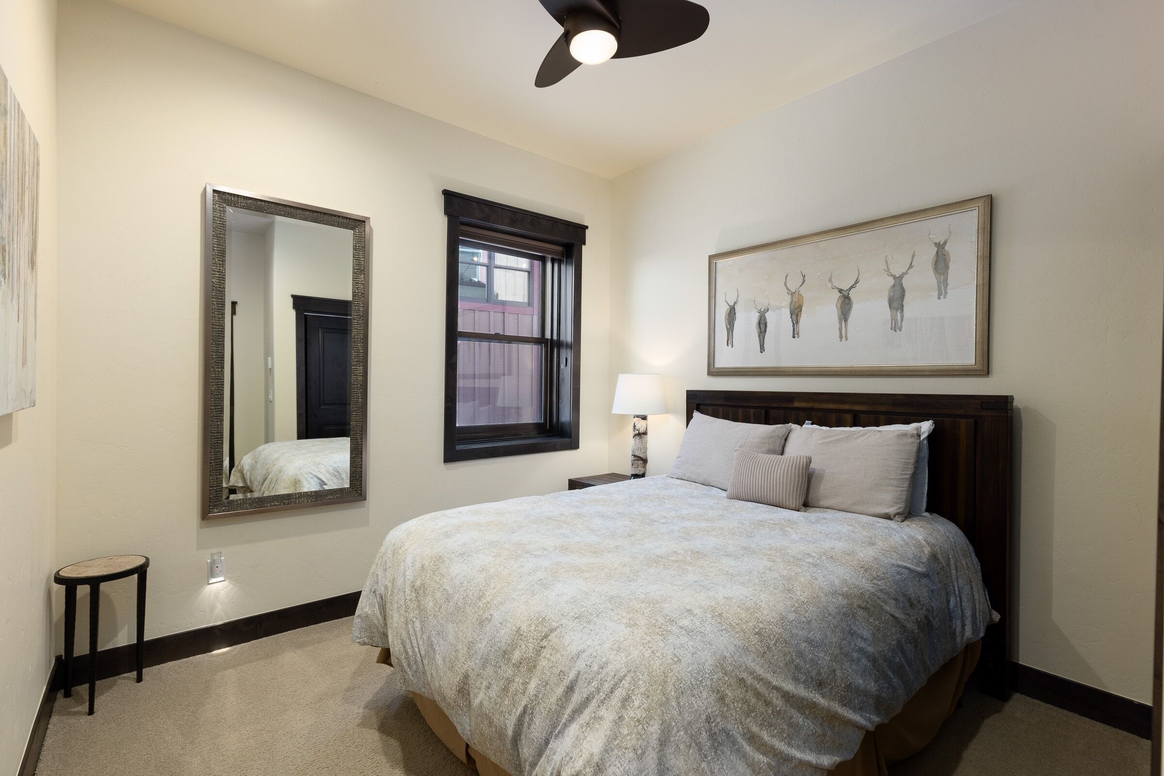 Une chambre à coucher avec un grand lit, un ventilateur de plafond, une fenêtre, un miroir et une œuvre d’art encadrée accrochée au mur.