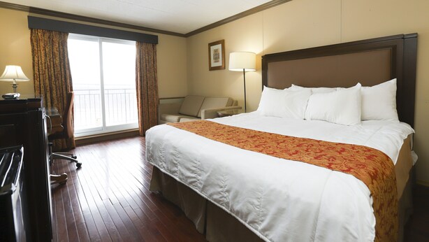 A hotel room with a large bed, a desk, a chair, and a window with curtains. - Owen Sound Inn (Owen Sound)