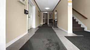 A hallway with a carpet, a door, a wall-mounted phone, and a staircase. - Owen Sound Inn (Owen Sound)