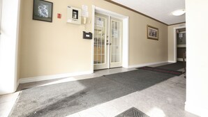 A hallway with a door, a phone, a sign, and a framed picture on the wall. - Owen Sound Inn (Owen Sound)