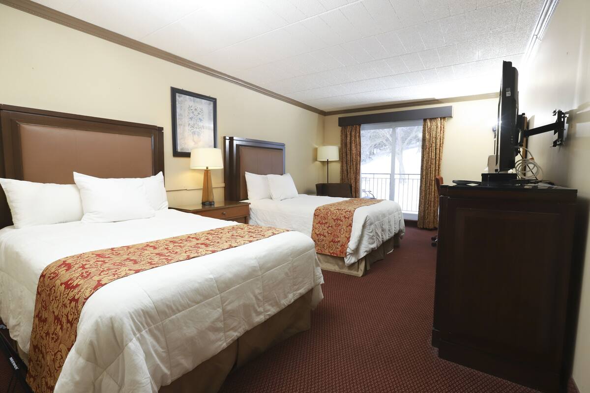 A hotel room with two beds, a desk, a television, and a window with curtains.