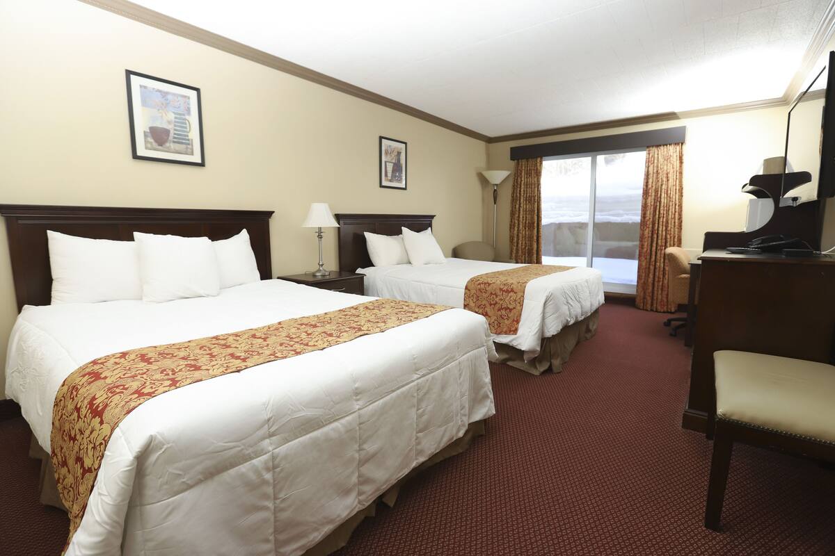 A hotel room with two beds, a desk, a chair, and a large window with curtains.