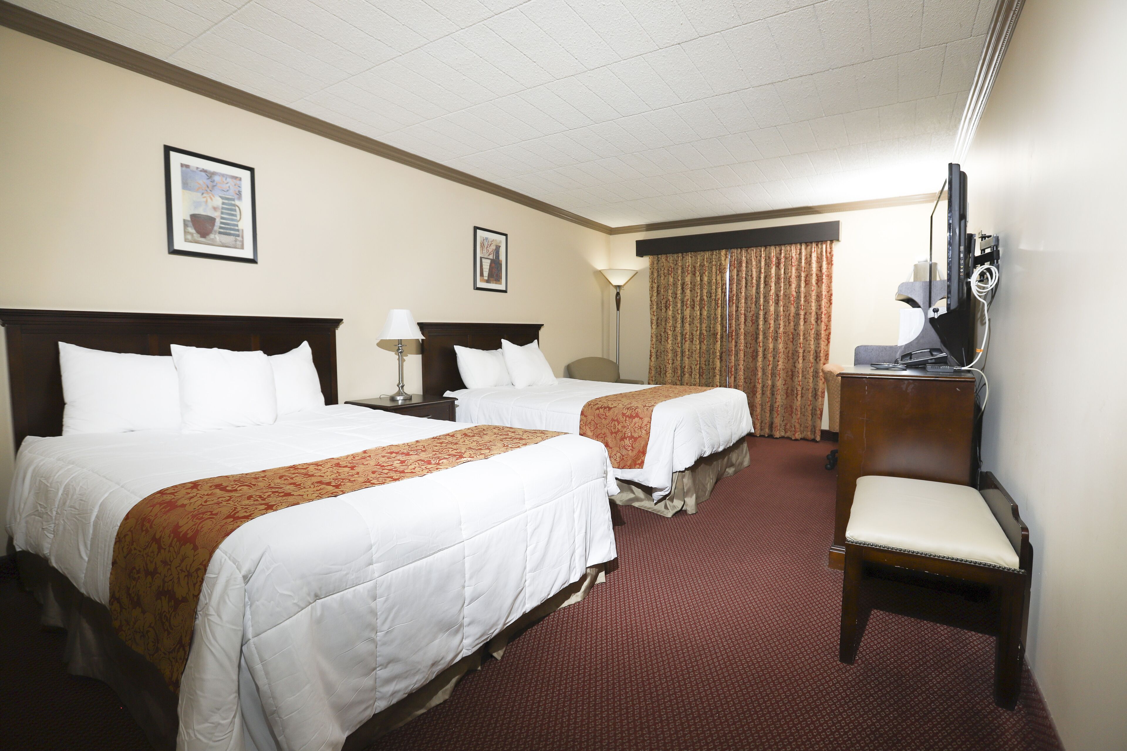 A hotel room with two beds, a desk, a chair, a TV, and a window with curtains.