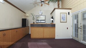 A hotel room with a wooden cabinet, a ceiling fan, a clock, a mirror, a plant, and a door with blinds. - Owen Sound Inn (Owen Sound)
