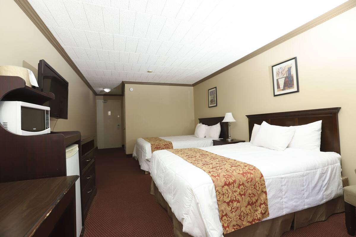 A hotel room with two beds, a desk with a microwave, a TV, and a framed picture on the wall.
