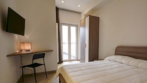 A bedroom with a bed, a desk, a chair, a TV, and a sliding door to a balcony. - Appartamento Ariel   La Perla del Mare di Polignano (Polignano a Mare)