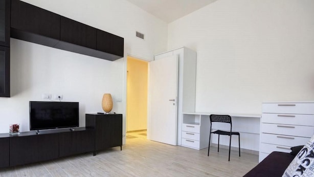 A modern living room with a flat-screen TV, a black entertainment unit, a white desk with a chair, and a wardrobe. - Appartamento Ariel   La Perla del Mare di Polignano (Polignano a Mare)