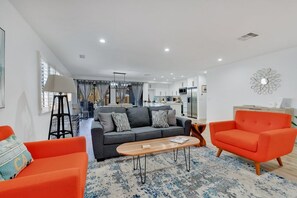 A modern living room with a sofa, armchairs, a coffee table, and a dining area with a kitchen in the background.