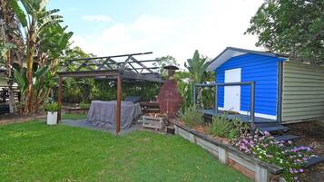 Un patio trasero con un pérgola de madera, una zona de barbacoa y un cobertizo azul.
