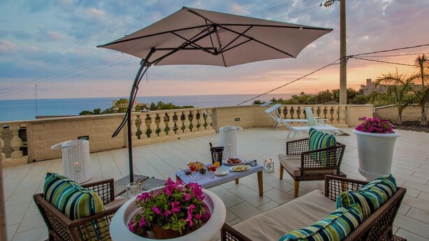 Une terrasse extérieure avec une table dressée pour les repas, des meubles en osier et un grand parasol offrant de l’ombre.