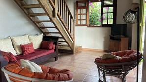 Un salon avec un escalier en bois, un canapé agrémenté de coussins à motifs, un fauteuil en osier et un téléviseur posé sur un meuble en bois.