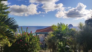 Une vue sur la côte, avec un bâtiment doté d’un toit recouvert de tuiles rouges, entouré d’une végétation luxuriante et de plantes en fleurs.